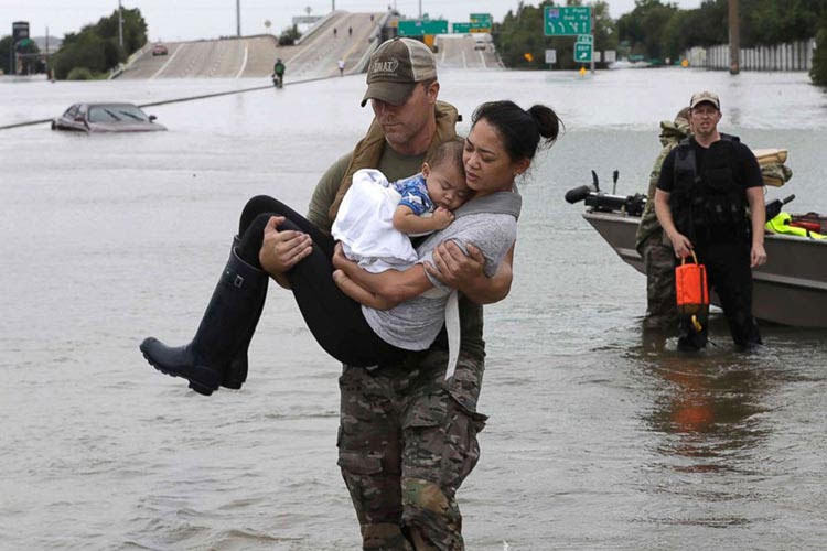 image of man carrying mother and baby, flood victims of hurricane harvey