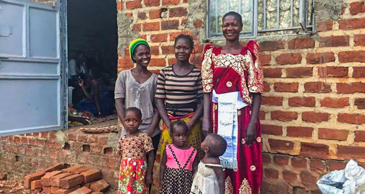 Picture of Christine, a former victim of sexual violence in DR Congo, with her family in front of their finished house